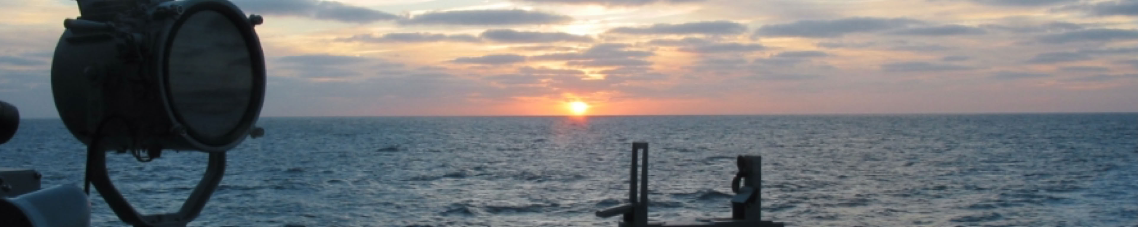 Sunset at sea, as seen from a Dutch Multi Purpose Frigate (M-Frigate) with a compass and signal light on the foreground.